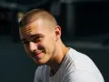 Joven sonriente con un corte afeitado impecable y barba cuidada, luciendo una camiseta blanca.