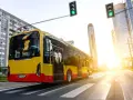 Żółto-czerwony autobus elektryczny Yutong jedzie przez miasto w blasku zachodzącego słońca.