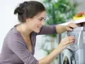 Lächelnde Frau stellt ein Programm an der Waschmaschine ein, um sie zu entkalken.