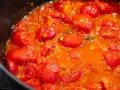 Ein köstliches, blubberndes Tomaten Sugo in einer schwarzen Pfanne, voller saftiger Kirschtomaten und aromatischer Kräuter.