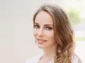 Uśmiechnięta kobieta z mysi blond włosami, delikatnie falującymi na ramionach.