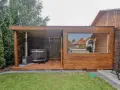Drewniany domek z sauną i beczką do kąpieli, z piecem zewnętrznym i prysznicem. Duże okno wychodzi na ogród.