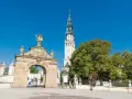 Brama na Jasną Górę, gdzie pielgrzymi zastanawiają się, ile ma lat to miejsce o bogatej historii. Wieża klasztoru góruje nad zielenią.