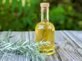 Eine kleine Glasflasche mit gelblicher Flüssigkeit und einem Korkverschluss steht neben frischen Wermut-Zweigen auf einem Holztisch. Ein altes Wermut Rezept zum Nachmachen.