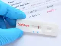 Rękawiczka ochronna trzyma test antygenowy COVID-19 z pozytywnym wynikiem.