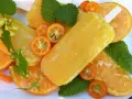 Paletas de helado de naranja, rodajas de naranja y kumquats adornan esta refrescante escena veraniega.