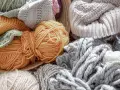 Ovillos de lana y tejidos de punto en tonos tierra y grises. El suave **merino material** invita a crear prendas cálidas y acogedoras.