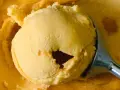 Ein Löffel hebt eine Kugel cremiges Sanddorn-Eis aus einer Schüssel. Die Farbe erinnert an die Sonne.