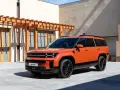 Pomarańczowy Hyundai Santa Fe, jeden z najlepszych SUV-ów, parkuje przed nowoczesnym budynkiem z drewnianą pergolą.