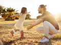 Ein kleines Mädchen rennt mit offenen Armen auf ihren lachenden Vater zu. Die warme Abendsonne beleuchtet die Szene und unterstreicht die liebevolle vater tochter beziehung.