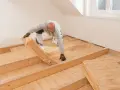 Mann verlegt Dämmmaterial auf Holzbalkendecke, vorbereitend für Estrich.