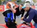 Giovane motociclista donna con casco e protezioni, ascolta i consigli di due uomini.