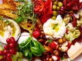 Eine Platte mit geilen Snacks: Hummus, Burrata, Trauben, Brot, Oliven, Pilze, Tomaten und Käse.