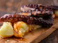 Pulpo tierno con patatas cocidas y espolvoreado con pimentón, servido en tabla de madera.