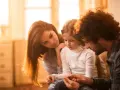 Eltern psychisch kranker Kinder spenden Trost. Ein Vater hält die Hände seiner Tochter, während die Mutter sie zärtlich berührt.
