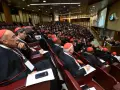 Wielu kardynałów w czerwonych biretach i czarnych szatach siedzi w amfiteatrze, słuchając przemówienia podczas ważnego konsystorza.