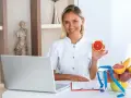 Uśmiechnięta dietetyczka z grejpfrutem w dłoni, obok laptopa i misy owoców. Chcesz wiedzieć, jak zostać dietetykiem?
