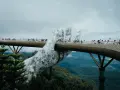 Goldene Brücke in Vietnam, gehalten von einer riesigen Steinhands. Touristen spazieren über die Brücke, die sich durch üppige grüne Berge schlängelt.