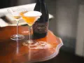 Dwa kieliszki koktajlowe z pianką i butelka kombuchy na drewnianym stole. Czy kombucha ma alkohol? Ta butelka sugeruje, że może mieć.