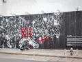 Une fresque murale de street art d'origine, "The Gun Chronicles: A Story of America", par JR x TIME, dépeint une foule en noir et blanc avec des touches de rouge vif.