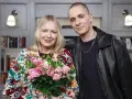 Mikołaj Krajewski z bukietem róż w dłoniach, obok uśmiechniętej kobiety w kolorowym żakiecie.