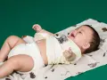 Uśmiechnięte dziecko w pieluszce tetrowej leży na kocyku. Pokazujemy, jak założyć pieluchę tetrową dziecku.