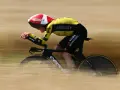 A cyclist in a yellow and black suit, helmet, and aero bars races during the Dauphine cycling event, blurring past the camera.