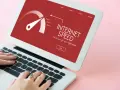 Schermo di un laptop con indicatore di velocità internet su sfondo rosso. Le mani digitano sulla tastiera, frustrati dall'internet lento.