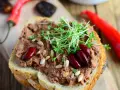 Pyszna pasta z czerwonej fasoli na chlebie, ozdobiona kiełkami i nasionami. Obok leżą papryczki chili.