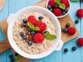 Un tazón de avena con frambuesas, arándanos y pasas. Descubre los beneficios de la avena por la noche para un descanso reparador.