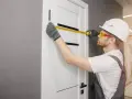 Fachowiec mierzy drzwi, przygotowując opaskę maskującą do ościeżnicy.