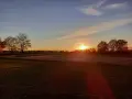 Sonnenuntergang über einem Feld mit Bäumen und einem Auto. "Seid stille und wisset: Ich bin Gott." (Psalm 46:10)