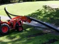 A tractor with a front loader is laying a long, flexible HDPE pipe across a grassy area.
