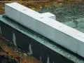 Białe bloczki betonowe układane na warstwie izolacji. Widać wilgotną zaprawę i ziemię wokół fundamentów.
