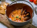 Un delicioso suquet de peix, con mejillones y gambas en una cazuela de barro, acompañado de tostadas.