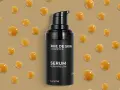 Czarny flakonik serum z alfa-arbutyną, otoczony kropelkami o bursztynowym kolorze.