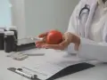 Lekarz trzyma w dłoniach czerwone serce, symbolizujące zdrowie. Na stole leżą leki i dokumentacja medyczna, sugerując rozmowę o tym, po jakim czasie spada cholesterol.