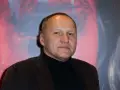 Portret Mariusza Grzegorzka w czarnym golfie i brązowej marynarce na tle abstrakcyjnego wzoru.