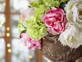 En bukett med rosa blomma, vita pioner och ljusgröna hortensior i en antik urn. Bakgrunden är mjukt suddig med ljus.