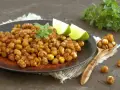 Ceci croccanti al forno, conditi con paprika e guarniti con basilico fresco e spicchi di lime, invitano a uno snack salutare e gustoso.