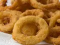 Knusprige zwiebelringe in der pfanne, goldbraun und perfekt frittiert, liegen auf einem weißen Küchentuch.