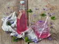 Flasche mit Veilchensirup und ein Glas mit Eis und Veilchenblüten auf Holzhintergrund.