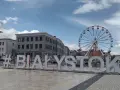 #Białystok - wielki napis zaprasza do odkrywania atrakcji miasta, w tle koło widokowe i zabytkowa zabudowa.