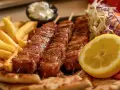 Pyszne souvlaki na patykach, podane z frytkami, pitą, surówką i cytryną.
