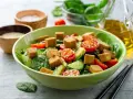 Kolorowa sałatka z chrupiącym tofu, pomidorkami koktajlowymi i ogórkiem na świeżym szpinaku.