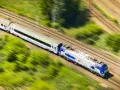 Pędzący pociąg PKP Intercity, model EU44 "Husarz", z białymi wagonami, mija zielone pola i drzewa.