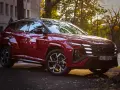 Czerwony Hyundai Tucson Hybrid zaparkowany na tle jesiennych drzew i kamienicy.