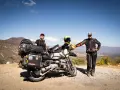 Para podróżników na motocyklu z bagażami, gotowych na przygodę. W tle górzysty krajobraz, idealny na corsyka motocyklem.