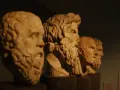 Bustos de mármol de filósofos de la edad antigua Grecia, con barbas y miradas serias, alineados en un museo.
