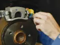 Mechanik dokręca śrubę w jarzmie zacisku hamulcowego, naprawiając układ hamulcowy pojazdu.